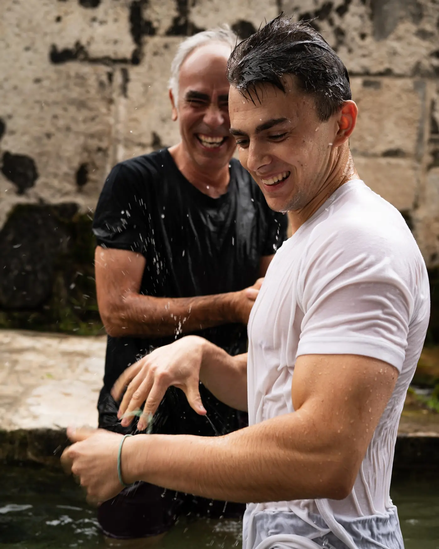 Un bautismo: dos hombres sonríen abrazados, empapados de agua